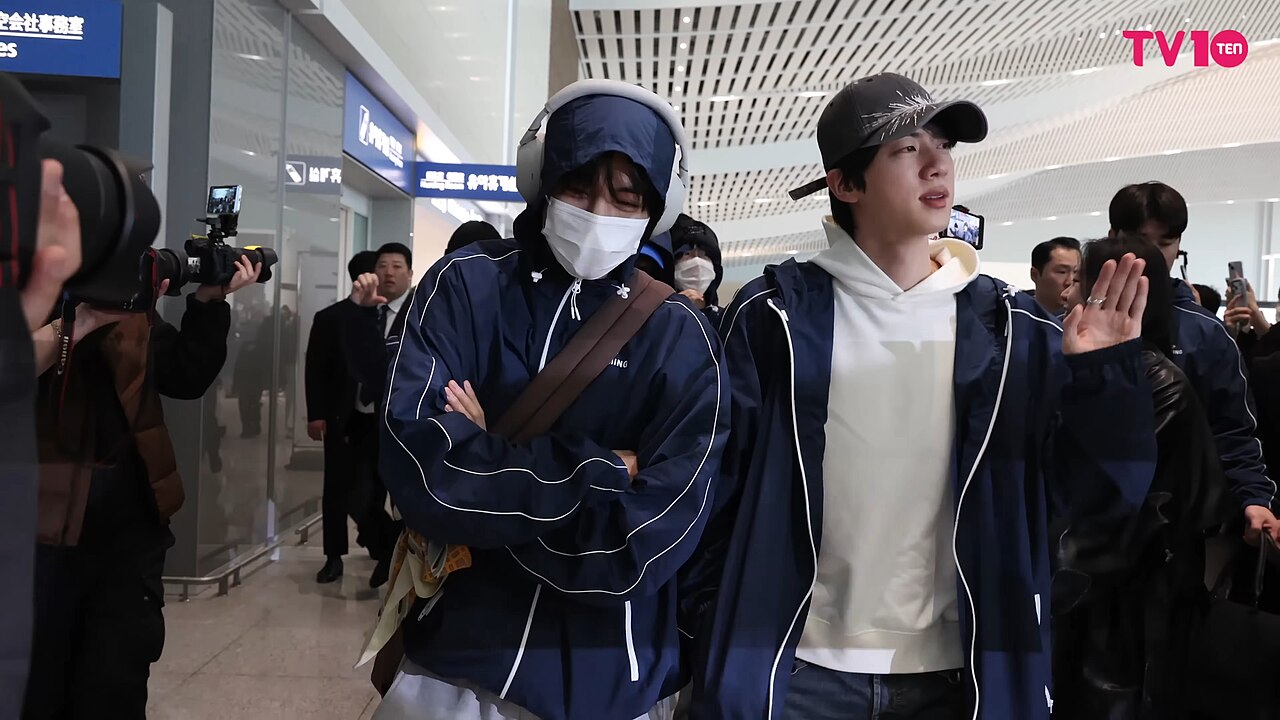 Jin de BTS saluda a su llegada al aeropuerto internacional de Incheon junto a otro miembro del grupo en 2026