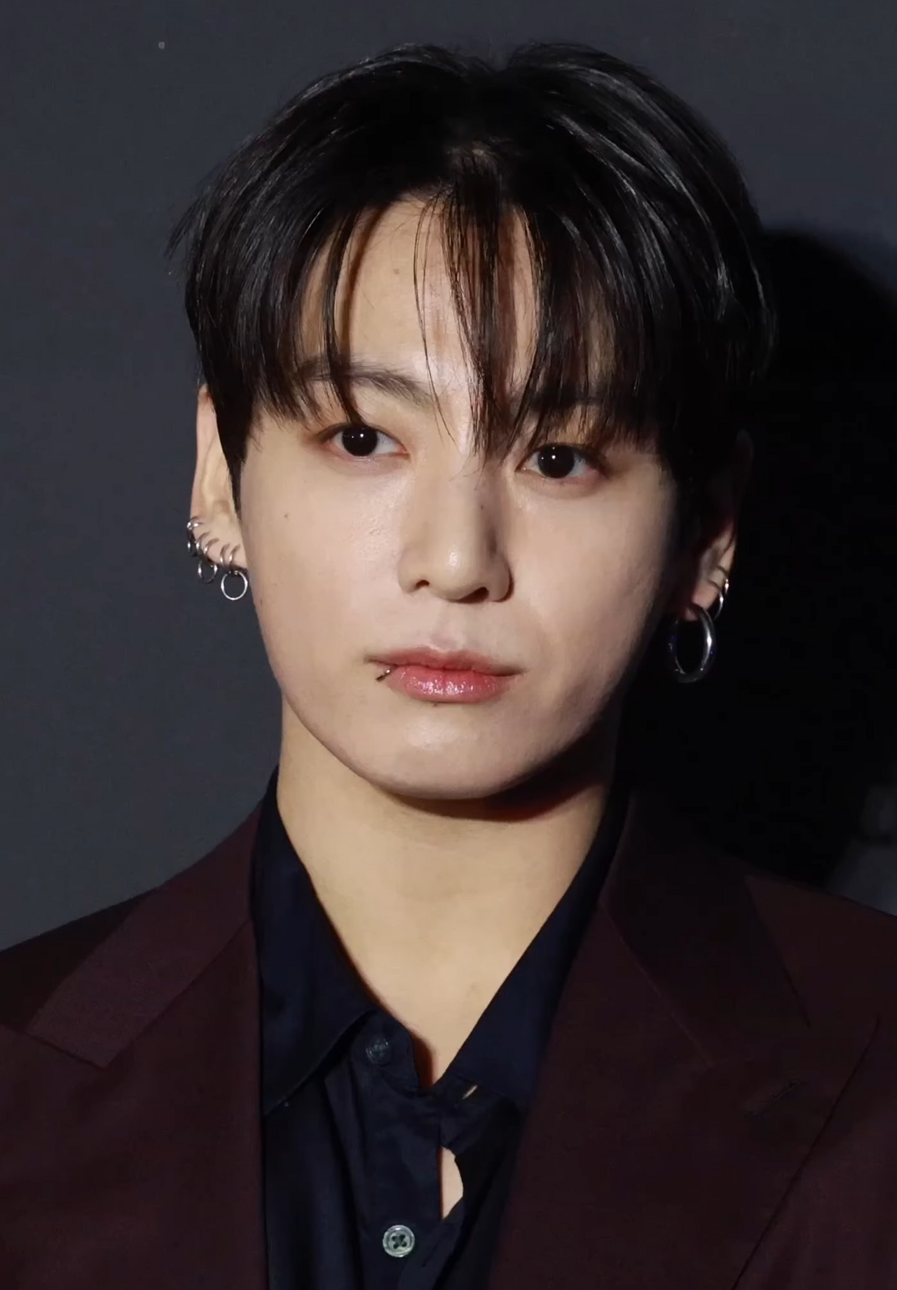 Retrato de Jung Kook de BTS con saco color vino y aretes plateados en un evento oficial de febrero de 2026