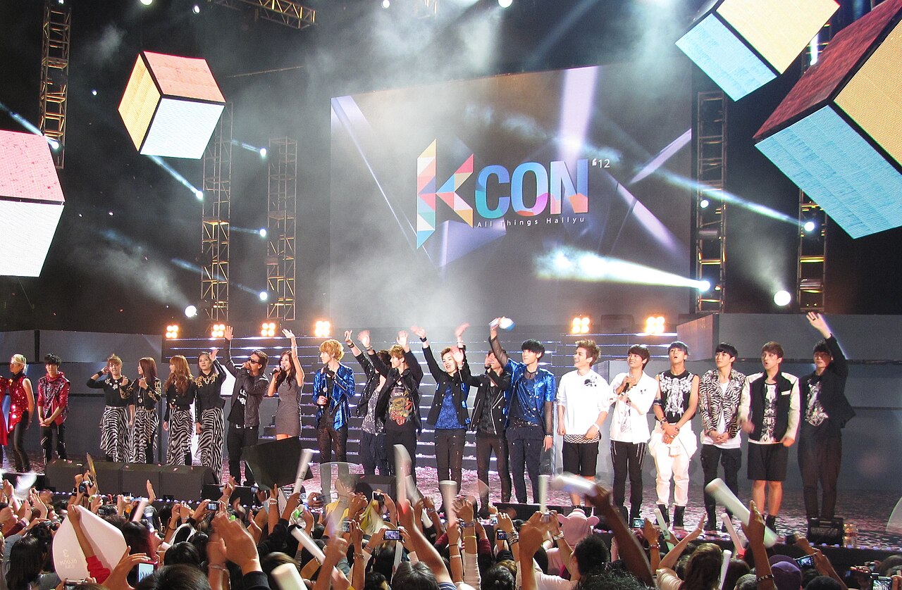 Varios grupos de K-pop saludan juntos en el escenario mientras el público los graba durante el festival KCON 2012