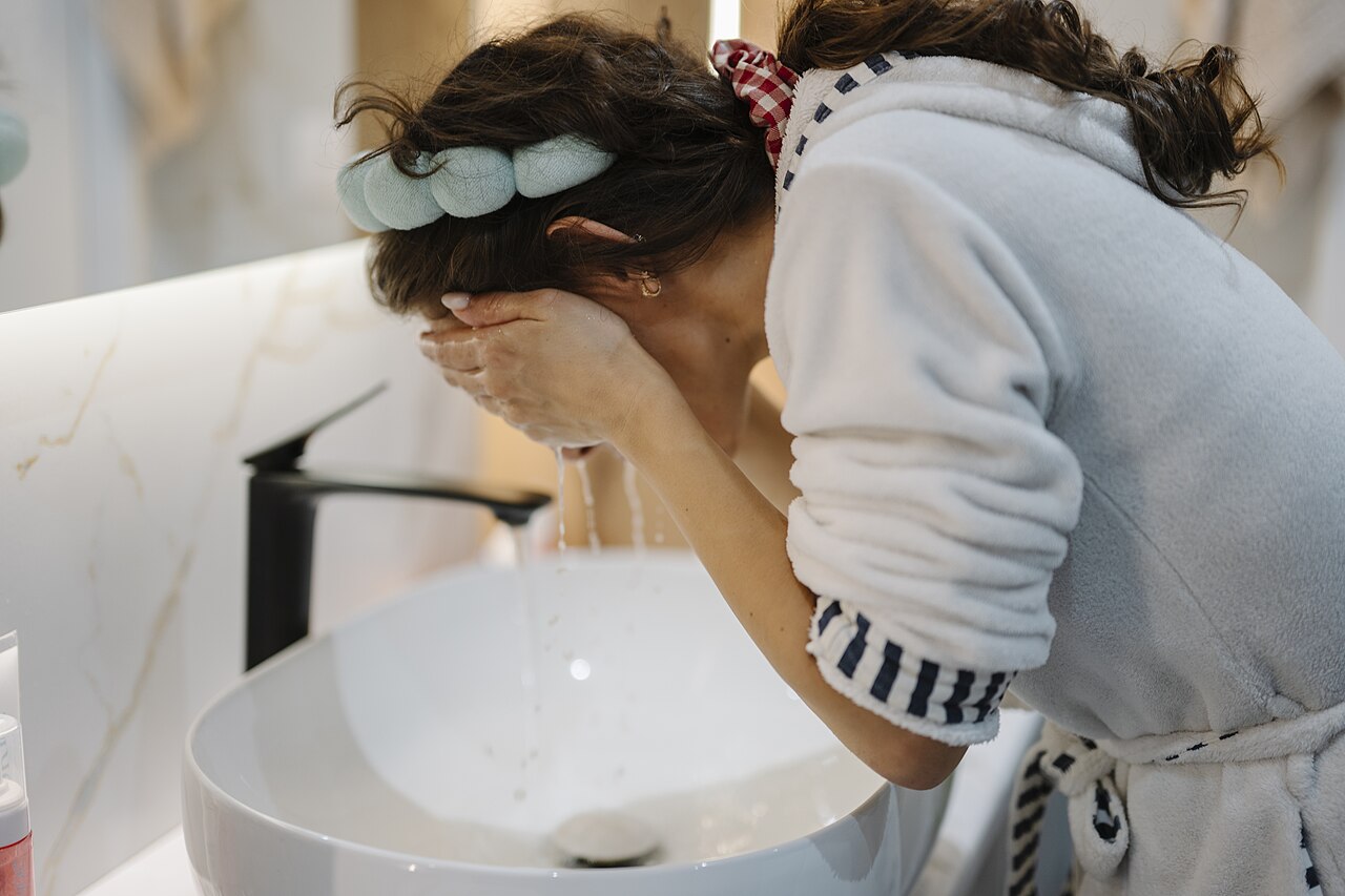 Mujer lavándose la cara en el lavabo del baño, el gesto central de la doble limpieza
